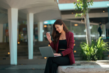 Asian woman waving during laptop video call outdoors