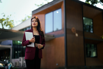 Asian businesswoman holding laptop walking in modern office park