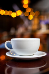 White Coffee Cup with Warm Lights Reflection in Cozy Café