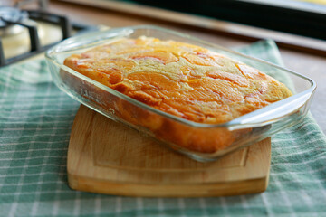 Peach cake in a glass dish on a wooden board on the kitchen counter