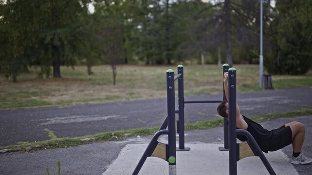 Two male friends train together in an outdoor park gym. They are performing dips on parallel bars, focusing on strength and physical fitness. This active lifestyle promotes health and wellness.