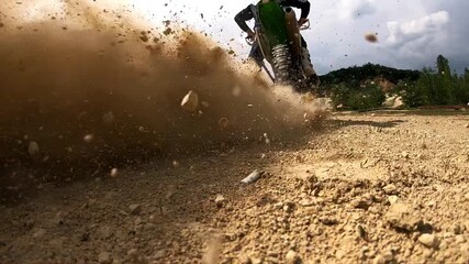 Motorcycle rider accelerates on dirt track, kicking up dust and showcasing powerful movement, with rugged terrain and trees framing the scene, capturing the thrill of off-road adventure