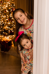 two little girls in pajamas by the Christmas tree at home on Christmas night
