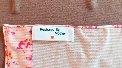Fabric label with restored by mother sewn onto floral cloth in closeup flatlay view