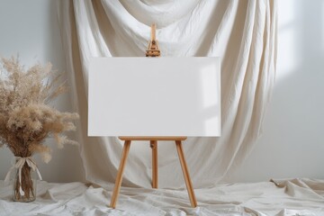Blank canvas on wooden easel stands in front of soft fabric backdrop, with dried flowers in a vase, creating a serene artistic atmosphere for creative projects
