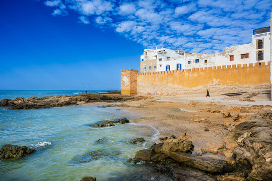 Rocky shore with a historic fort and blue sky by the sea, under fluffy white clouds.  Essaouira, Morocco