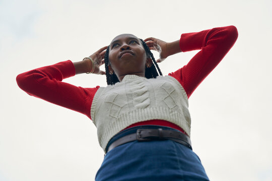Woman in red sweater and white vest looks up, standing against a cloudy sky. Bruges, Belgium