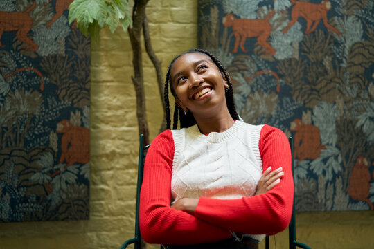 Smiling woman in a red and white sweater, seated with arms crossed, against a mural wall. Bruges, Belgium