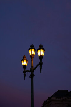 Three vintage street lamps glow warmly against a deep twilight sky backdrop. Blankenberge, West Flanders, Belgium