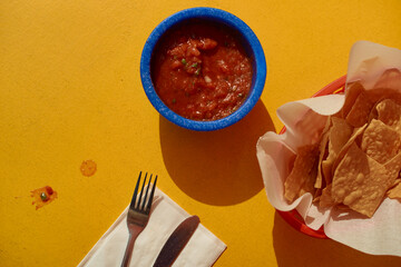 Top view of chips with salsa in vibrant blue bowl on bright yellow background. California, USA