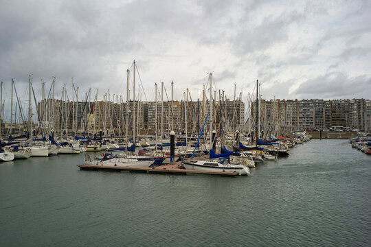 Numerous sailboats docked in a marina with overcast sky and urban background. Blankenberge, West Flanders, Belgium