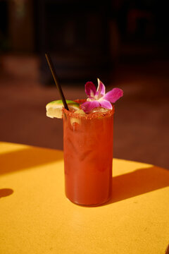 A red cocktail garnished with a lime slice and pink flower on a yellow table. California, USA