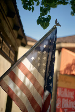 American flag waving on a pole with tree leaves and building in the background. California, USA