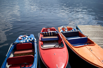 Three colorful rowboats docked on a serene lake with blue, red, and orange hulls. Salzkammergut, Salt Domain, Dachstein Mountains, Austria