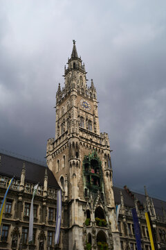 Gothic-style clock tower under a dramatic cloudy sky with flags adorning the building. Munich, Germany