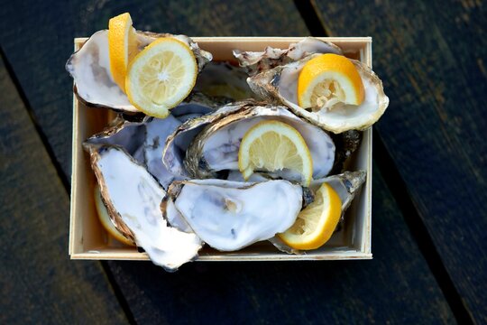 Fresh oysters and lemon slices arranged in a wooden box on a rustic wooden surface.