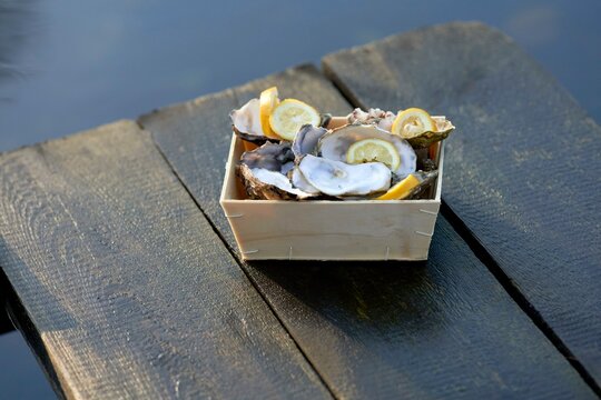 Fresh oysters and lemon slices arranged in a wooden box on a rustic wooden surface.