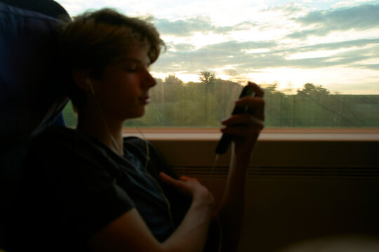Teenager on a train listening to music at sunset. Munich, Germany