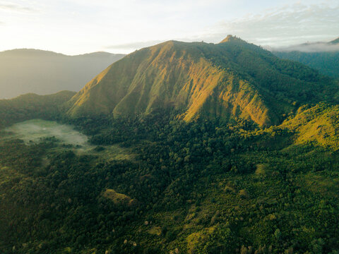 Aerial view of a lush green mountain range bathed in golden sunlight during the day. Lombok, Senaru, Indonesia