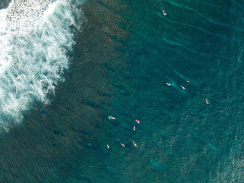 Aerial view of surfers in deep blue ocean with white crashing waves near a coral reef. Lombok, Semeti, Indonesia