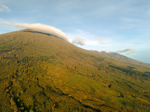 Lush green mountainside with clouds rolling over the peak under a blue sky. Lombok, Senaru, Indonesia