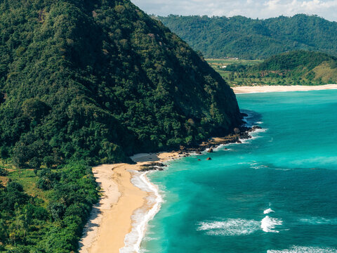 Tropical beach with turquoise waters and lush green hills under a clear blue sky. Lombok, Resto Nine, Indonesia