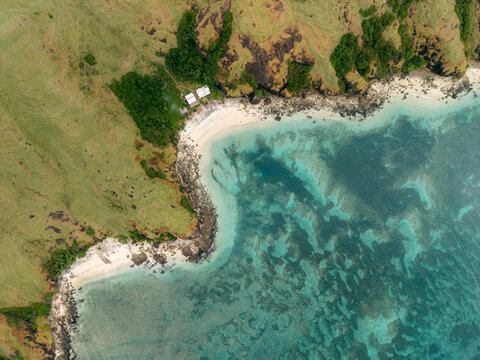 Aerial view of a pristine beach with turquoise waters and lush greenery on rocky terrain. Lombok, Tanjung Ann, Indonesia