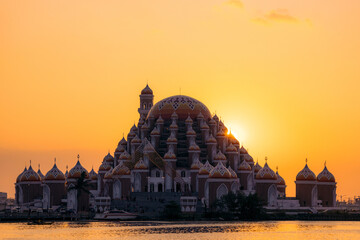 Majestic orange-domed mosque silhouette against a vibrant sunset over calm waters. Makassar, Sulawesi, Indonesia