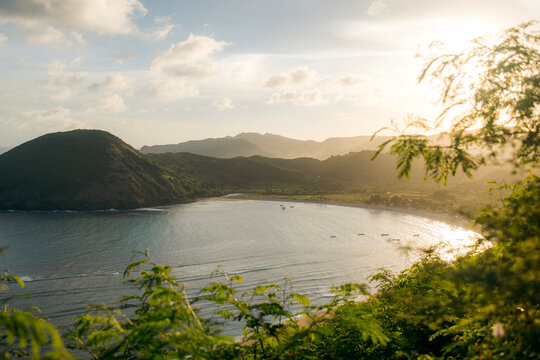 Serene coastal landscape with gentle waves and lush green hills under a glowing sunset sky. Lombok, Mawun, Indonesia