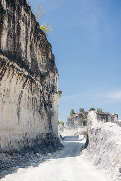 Narrow road cutting through towering white rock formations under a clear blue sky. Madura, East Java, Indonesia