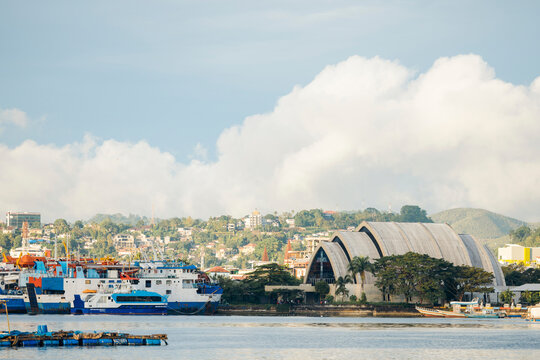 Coastal cityscape with large ships docked and hills in the background under a cloudy sky. Ambon, Maluku, Indonesia