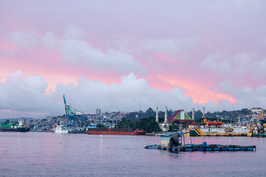 A vibrant sunset over a busy harbor with ships and colorful buildings on the shore. Ambon, Maluku, Indonesia