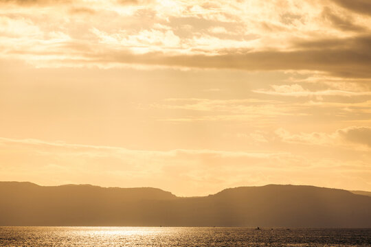 Golden sunset over calm ocean with silhouetted distant hills and cloudy sky. Ambon, Maluku, Indonesia