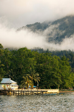 Misty forested mountains overlook a small lakeside dock and boathouse. Ambon, Maluku, Indonesia