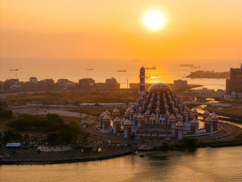 Mosque with vibrant domes at sunset near the sea, surrounded by water and cityscape. 99 Domes Mosque, Makassar, South Sulawesi, Indonesia
