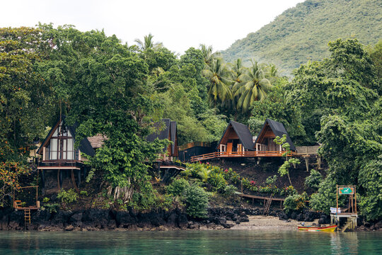 Scenic view of tropical wooden cabins nestled amidst lush greenery by a tranquil waterfront. Banda Neira, Banda, Central Maluku, Indonesia