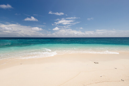 Pristine beach with white sand and clear turquoise ocean under a blue sky with clouds. Pulau Nailaka or Nailaka Island, Banda, Central Maluku, Indonesia
