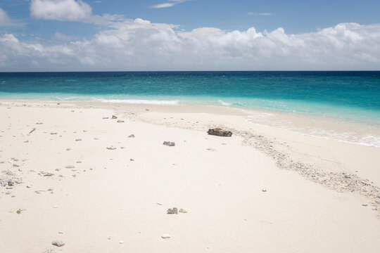 Pristine sandy beach with turquoise waves under a bright blue sky with scattered clouds. Pulau Nailaka or Nailaka Island, Banda, Central Maluku, Indonesia