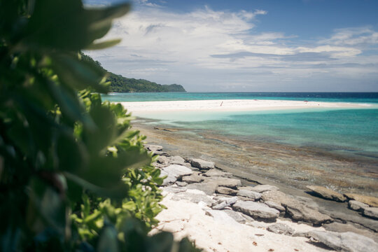 Pristine tropical beach with clear turquoise water and lush green foliage under a bright blue sky. Pulau Nailaka or Nailaka Island, Banda, Central Maluku, Indonesia