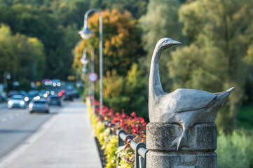Skulptur einer Gans Anserinae auf der Neckarbrücke mit fließendem Verkehr in Reutlingen Mittelstadt mit Blumenschmuck am Brückengeländer. 
