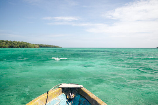 Boat in clear turquoise sea heading towards a distant green coastline under a blue sky. Pulau Bair or Bair Island in Kei Kecil, Southeast Maluku Regency, Maluku, Indonesia