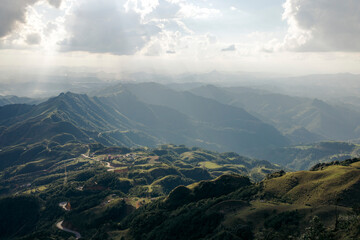 Sunlit mountains and valleys under a cloudy sky with rays of light streaming down. Loc BÏnh District, Lang Son, Vietnam