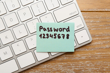Paper note with password and computer keyboard on wooden table, top view