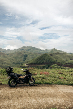 A motorcycle parked on a rural road against a backdrop of rolling green hills under a cloudy sky. Binh Lieu District, Quang Ninh, Vietnam