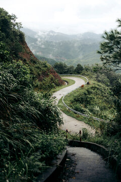 Winding mountain road amidst lush greenery with misty hills in the background. Binh Lieu District, Quang Ninh, Vietnam
