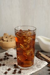Tasty coffee with ice in glass, beans and sugar cubes on wooden table against grey background, closeup