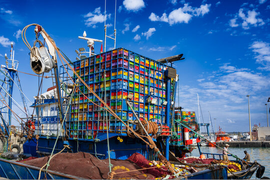 Fishing boats with colorful crates docked at a busy harbor under a clear blue sky.  Essaouira, Morocco