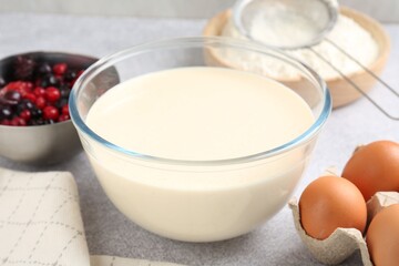 Liquid dough in bowl, berries and ingredients on light grey table, closeup