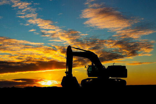 Silhouette of an excavator against a vibrant sunset sky with clouds. Calgary, Canada