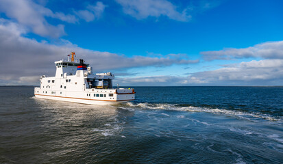 Car ferry with vacationers traveling from Norddeich Mole to Norderney (Germany) on the crossing through the Wadden Sea World Heritage. Atmospheric photograph in the evening light.